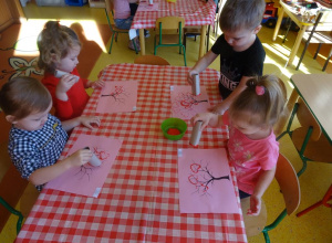 Czworo dzieci stempluje rolkami papierowymi w kształcie serca koronę drzewa.